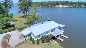 A large house with a dock extending into a lake, surrounded by lush greenery and a clear sky. - Lake Life Retreat 3BR Home w/ 2 Kitchens & Docks (Warwick)