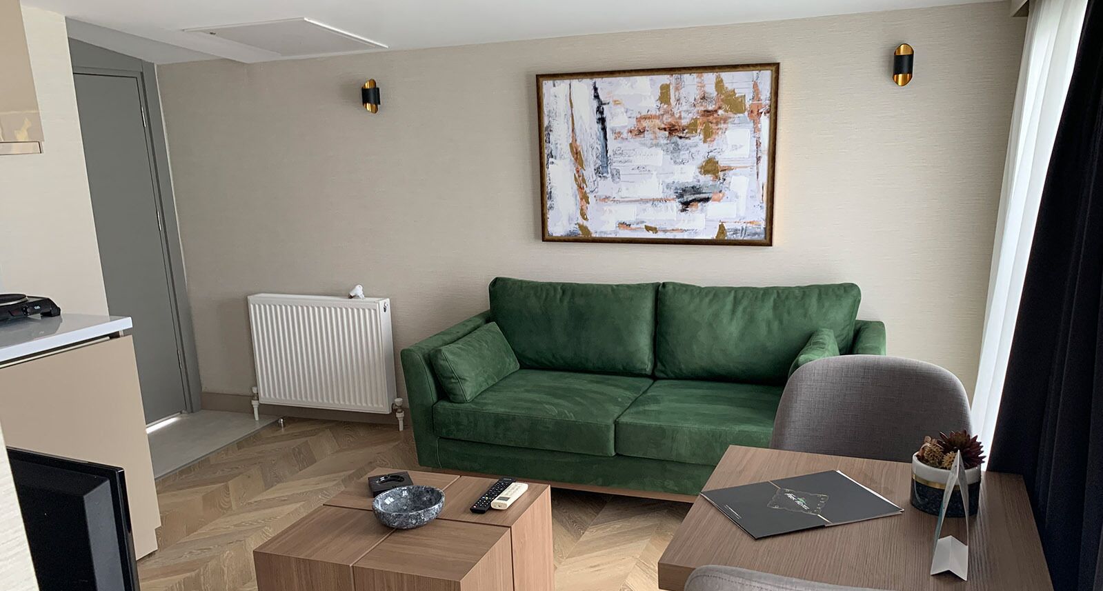 A modern living room with a green sofa, a wooden coffee table, a grey armchair, and a painting on the wall.