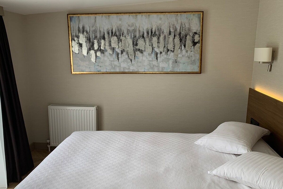 Een hotelkamer met een groot bed, een radiator, een wandlamp en een schilderij.