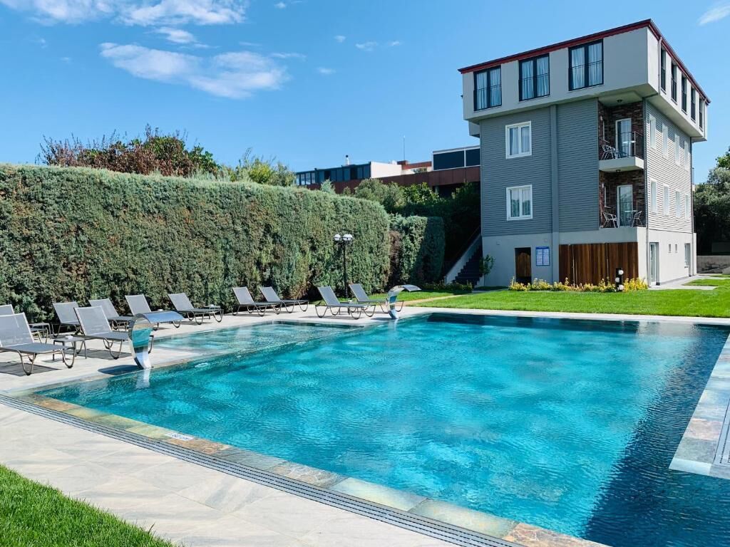 A modern building with a swimming pool, lounge chairs, and a well-maintained hedge.