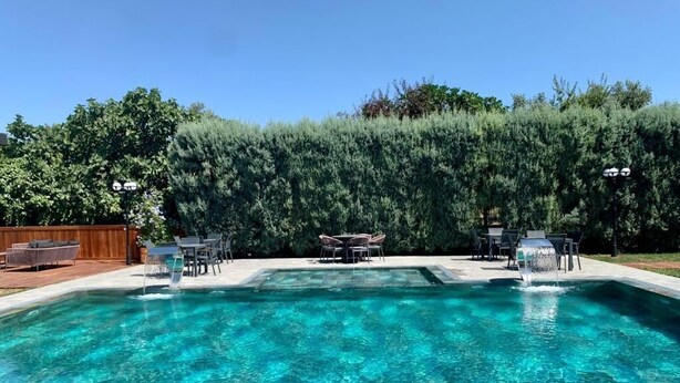 A rectangular swimming pool with clear blue water, surrounded by a wooden deck and a hedge. - Istanbul Park Hotel (Tuzla)