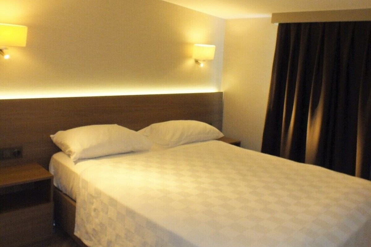 A hotel room with a single bed, two bedside lamps, a nightstand, and a window with curtains.