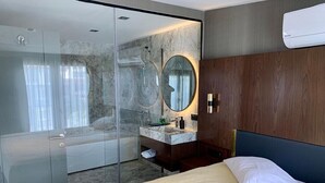 A modern hotel room with a glass-enclosed shower, a marble-topped vanity, and a bed with a dark headboard. - Istanbul Park Hotel (Tuzla)