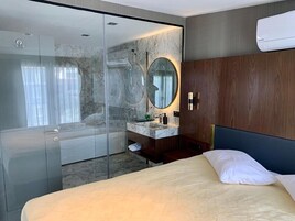 Una habitación de hotel moderna con ducha de vidrio, tocador de mármol y cama con cabecera oscura.
