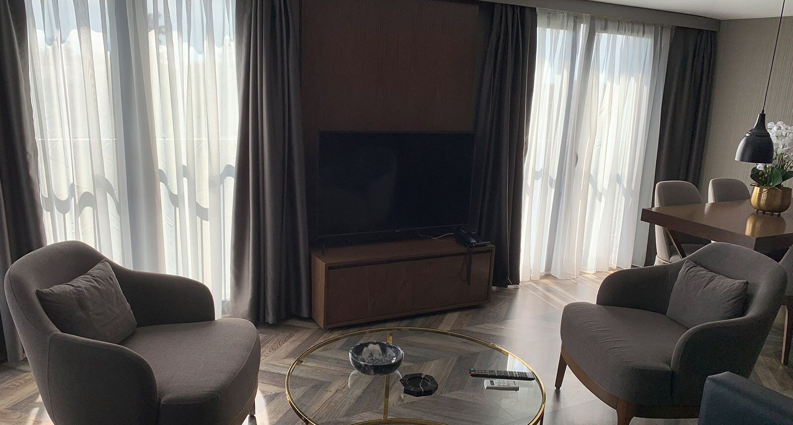 A modern living room with two armchairs, a coffee table, a flat-screen TV, and a dining area with a table and chairs.