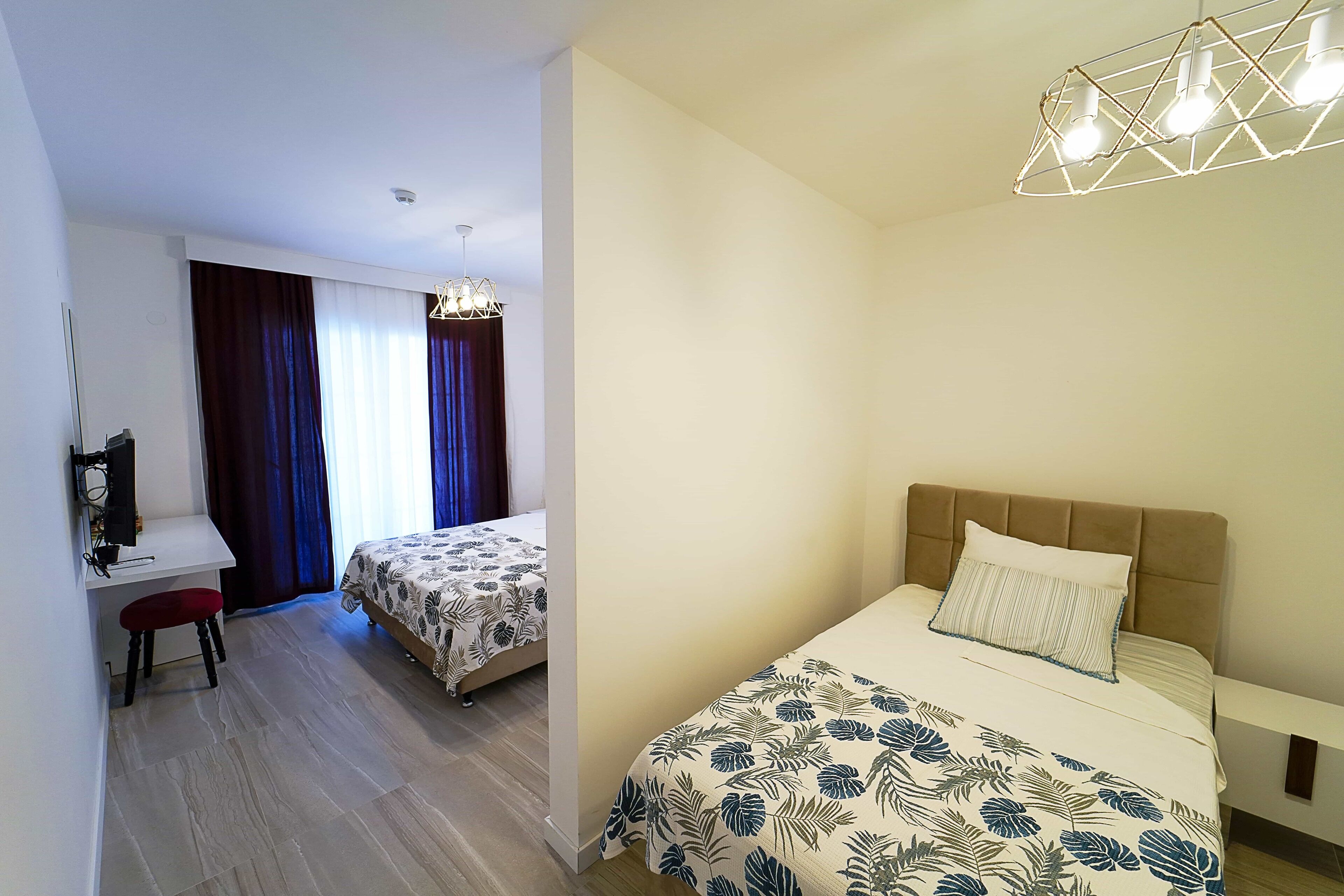 Habitación de hotel con cama, escritorio y silla. Se ve una ventana con cortinas y una lámpara en el techo.