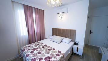 A modern bedroom with a bed, a nightstand, an air conditioning unit, and a door.
