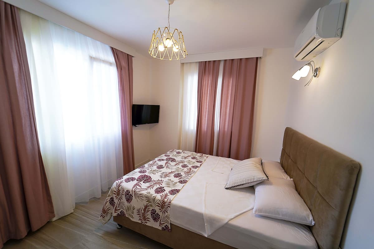 A bedroom with a bed, curtains, a mounted TV, and a ceiling light fixture.
