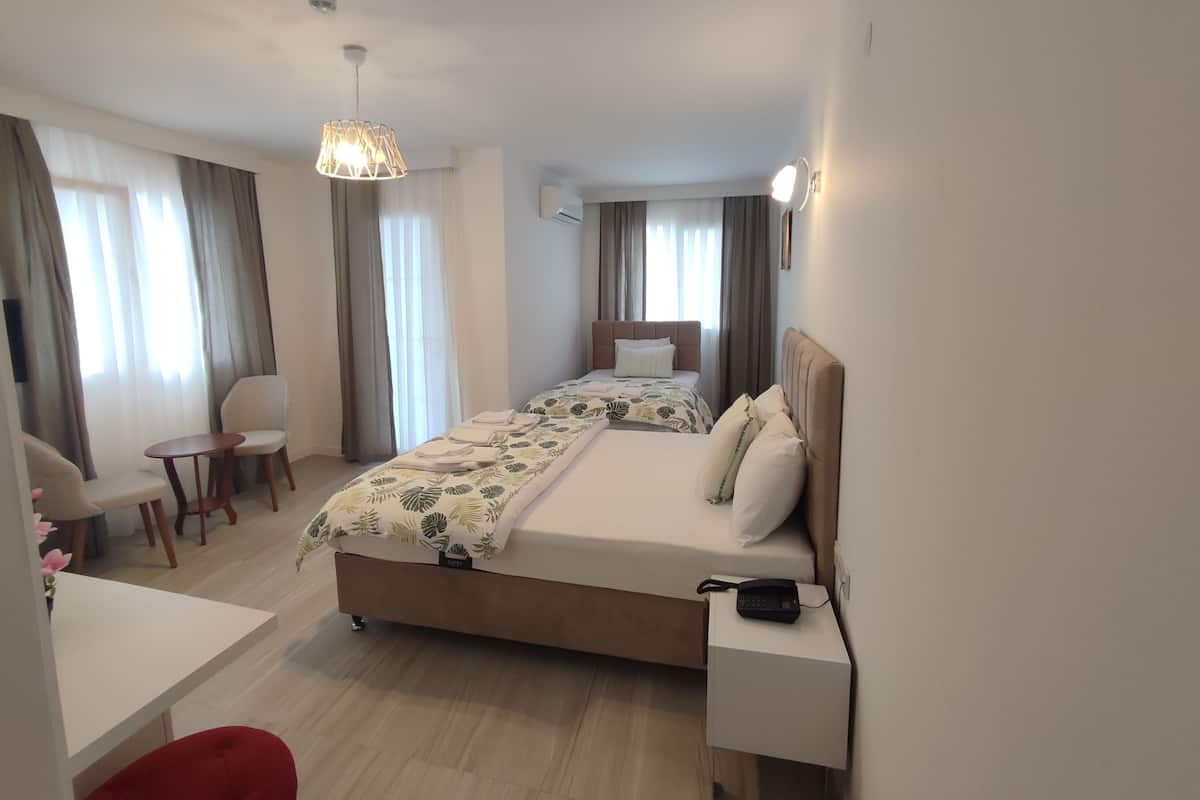 A hotel room with a bed, bedside table, chair, desk, and a hanging light fixture.