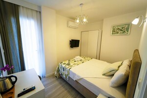 Habitación de hotel con cama, escritorio con tetera, control remoto y televisor montado en la pared.