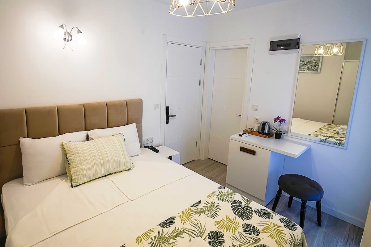 A bedroom with a bed, bedside table, desk, chair, and a mirror.