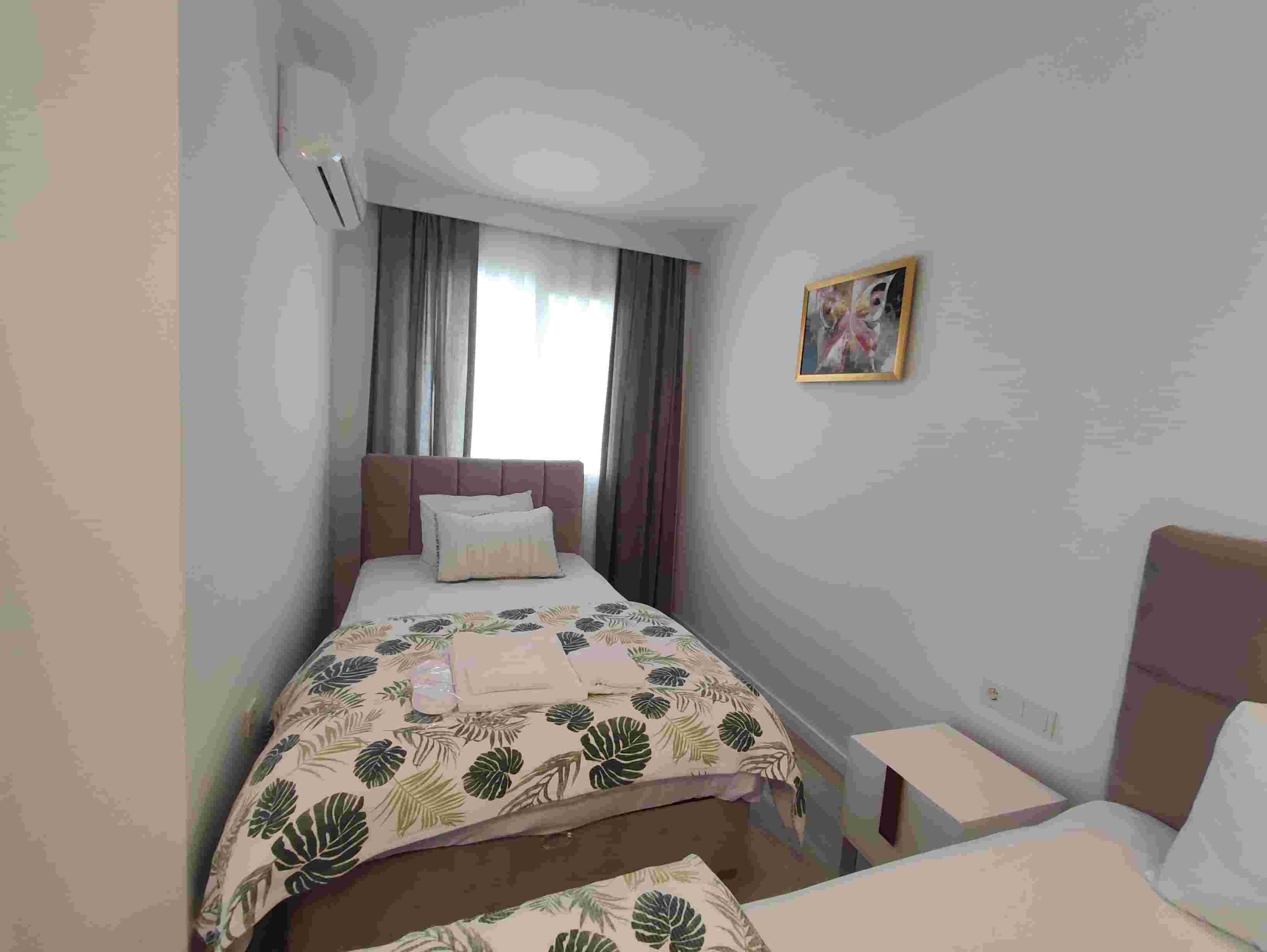 A bedroom with a bed, a nightstand, a painting, and an air conditioning unit.