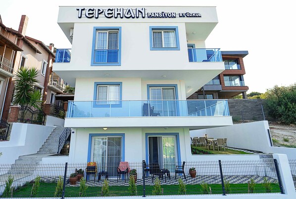 Un hôtel à plusieurs étages, doté d’un design moderne, comprenant des balcons, une terrasse avec des espaces salons extérieurs et un escalier menant à l’entrée.