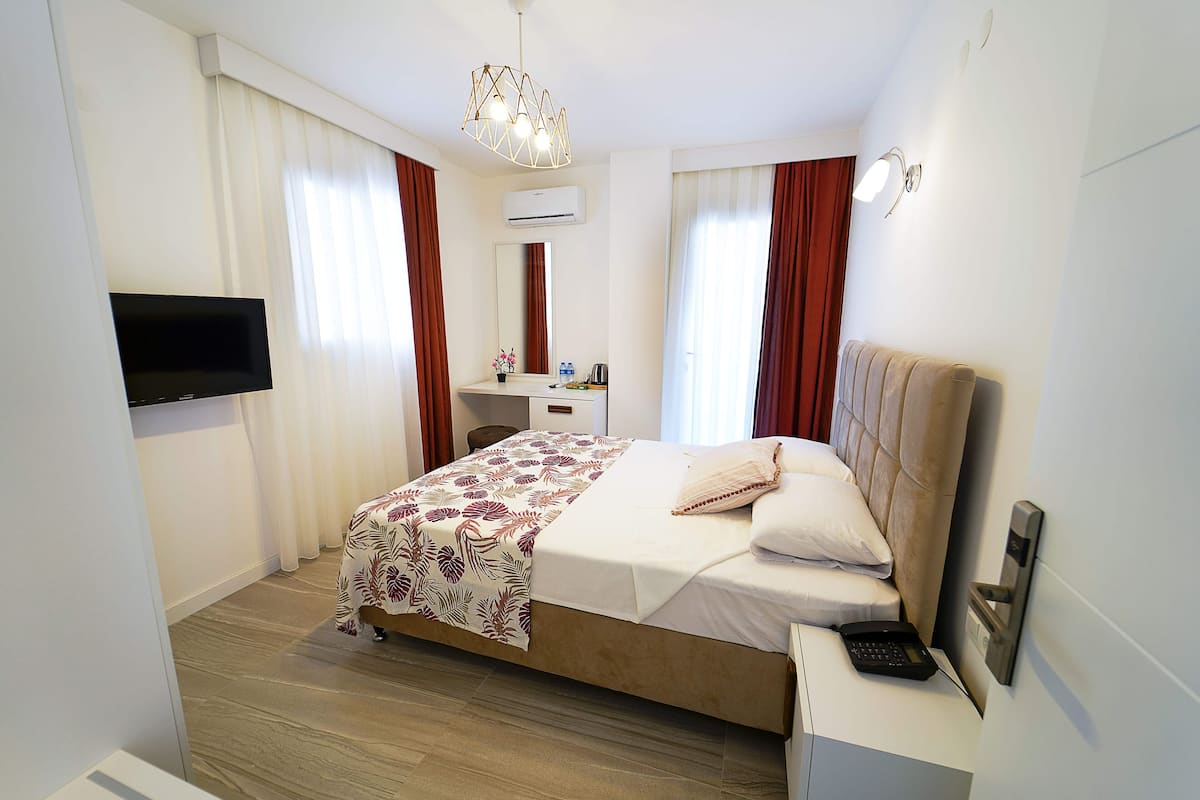 A hotel room with a bed, bedside table, TV, air conditioning unit, and a mirror.