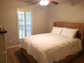Ein Schlafzimmer mit einem Bett, einem Deckenventilator und einem Fenster mit Jalousien.
