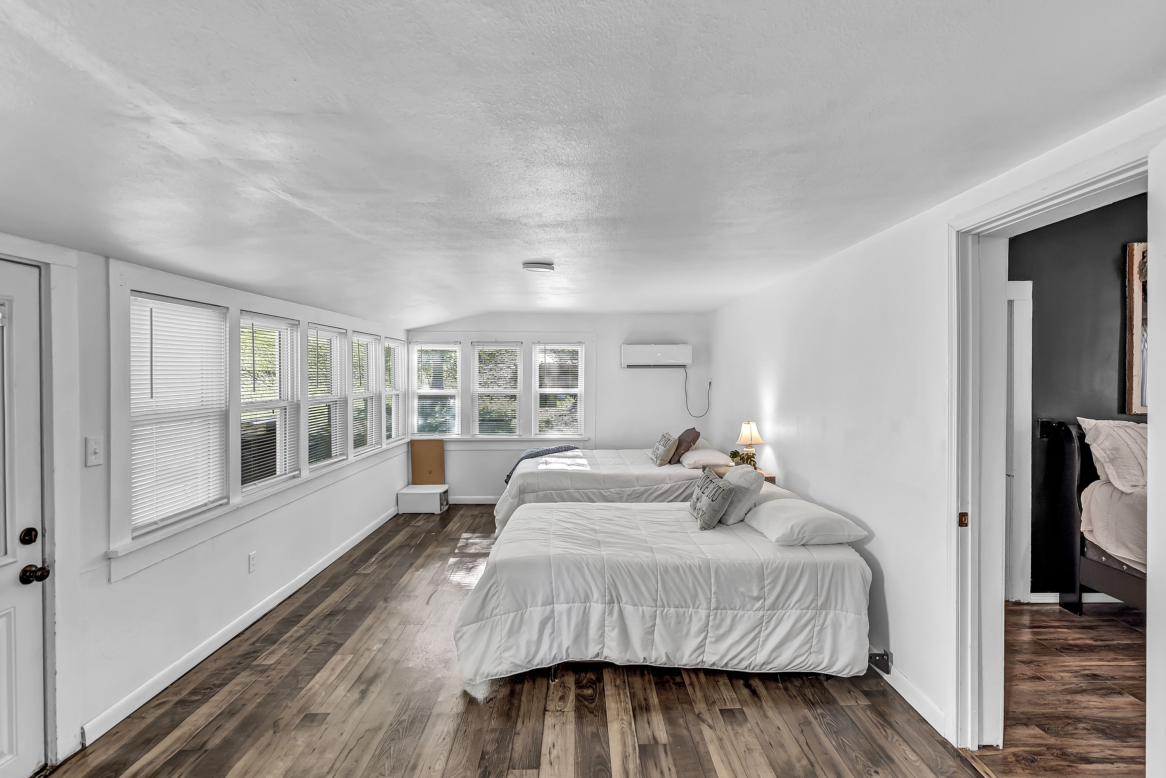 Ein Schlafzimmer mit zwei Betten, Holzboden, weißen Wänden und einem Fenster mit Jalousien.