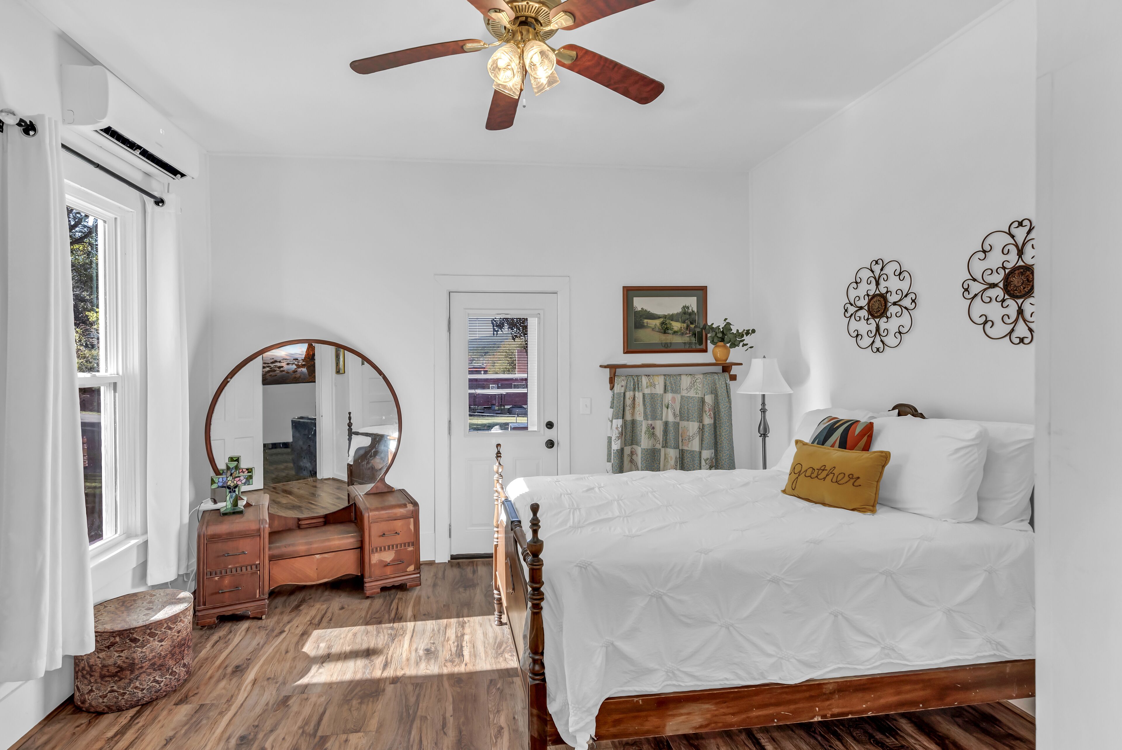 A bedroom with a wooden bed, a ceiling fan, a dresser, a mirror, and a door with a view of the outside.