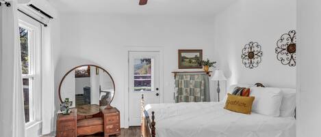 A bedroom with a wooden bed, a ceiling fan, a dresser, a mirror, and a door with a view of the outside.