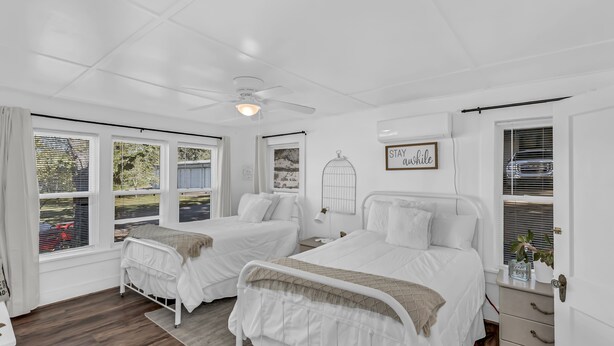Ein helles Schlafzimmer mit zwei Betten, einem Deckenventilator und einem Fenster mit Jalousien.