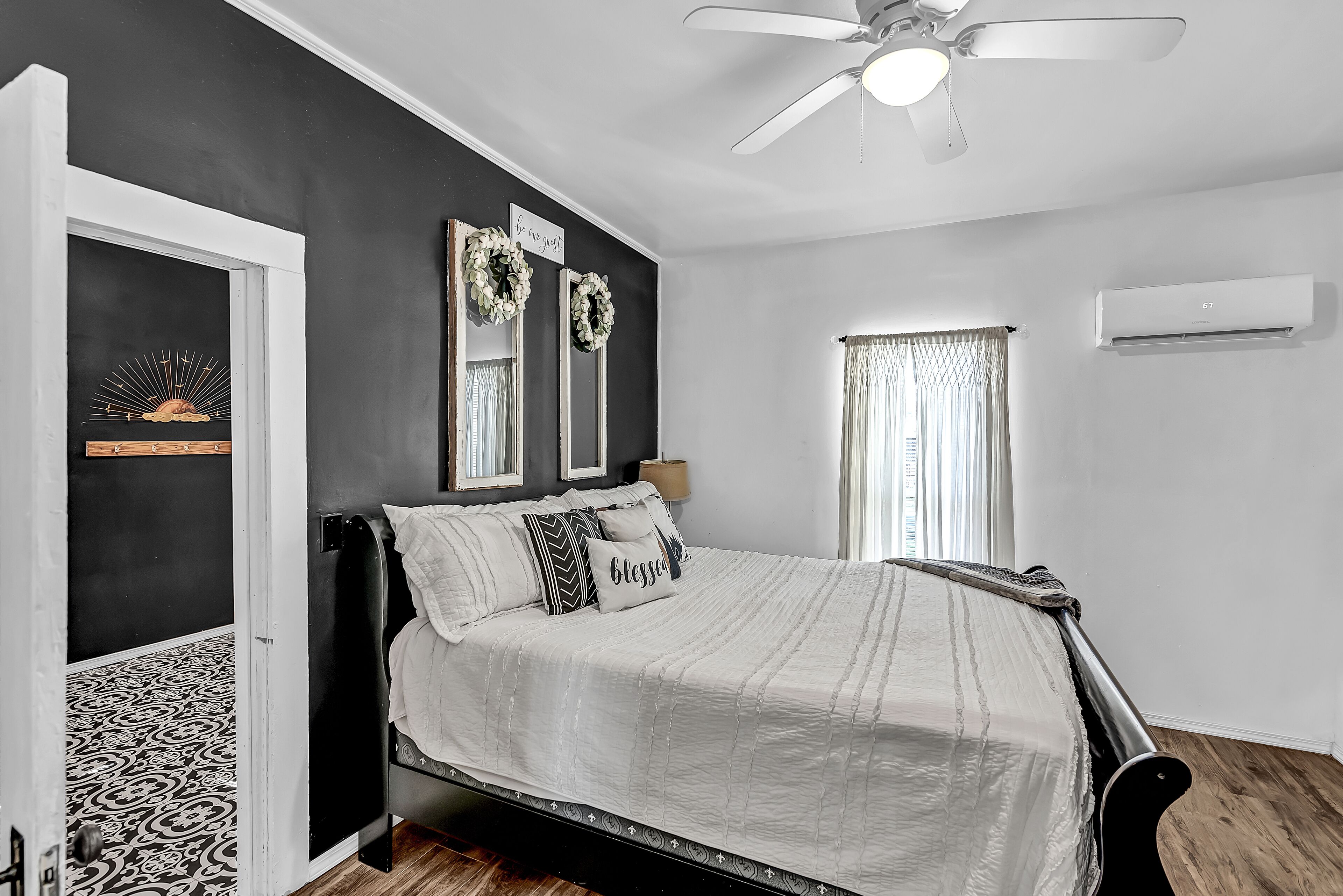A bedroom with a bed, a ceiling fan, a window with curtains, and a wall-mounted air conditioner.