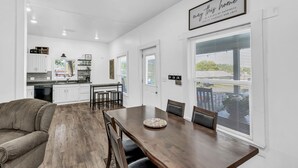 Eine moderne Küche mit weißen Schränken, eine Essecke mit einem Holztisch und Stühlen sowie ein gemütliches Wohnzimmer mit einem braunen Sofa.