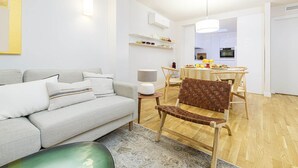 Un salón moderno con un sofá gris, una silla de madera y una mesa de comedor con mantel a cuadros.