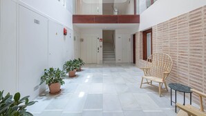 Un corredor amplio con una escalera que sube a un nivel superior, plantas en macetas y muebles de madera.