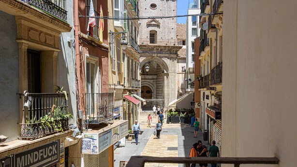 Una calle estrecha flanqueada por edificios, con la entrada de una iglesia a la vista y gente caminando.