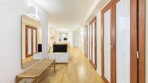 Un pasillo con pisos de madera, un banco, un espejo y un televisor al final de una habitación.