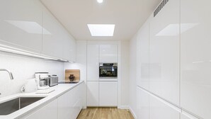 Una cocina moderna con armarios blancos, horno empotrado, cafetera y tabla de cortar de madera.
