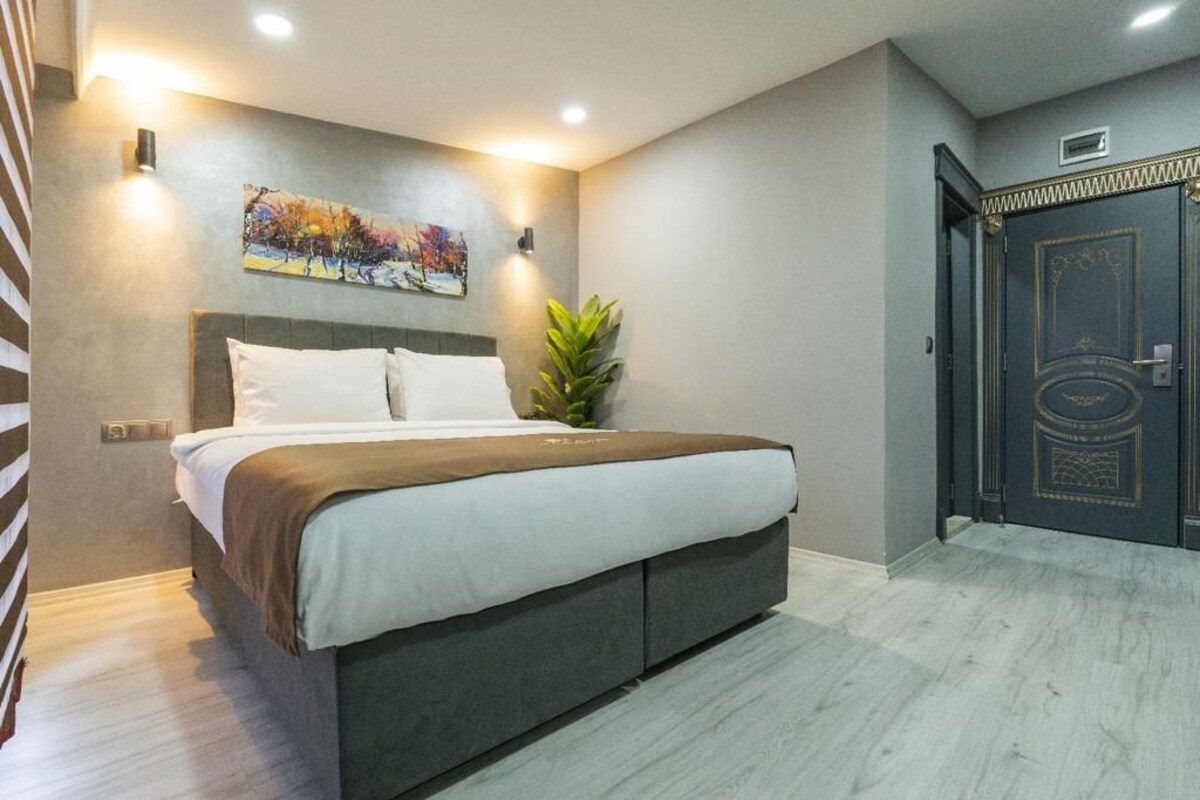 Een moderne hotelkamer met een groot bed, een schilderij aan de muur, een potplant en een donkere deur met ingewikkeld ontwerp.