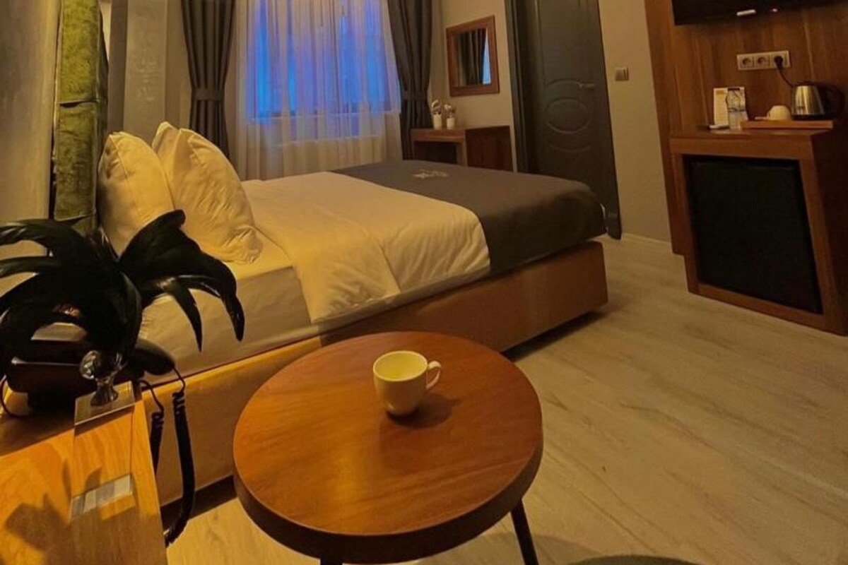 A modern hotel room with a bed, a small table with a cup, a TV, and a wooden desk.