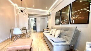 A modern living room with a grey sofa, a dining table with chairs, and a ceiling light fixture.