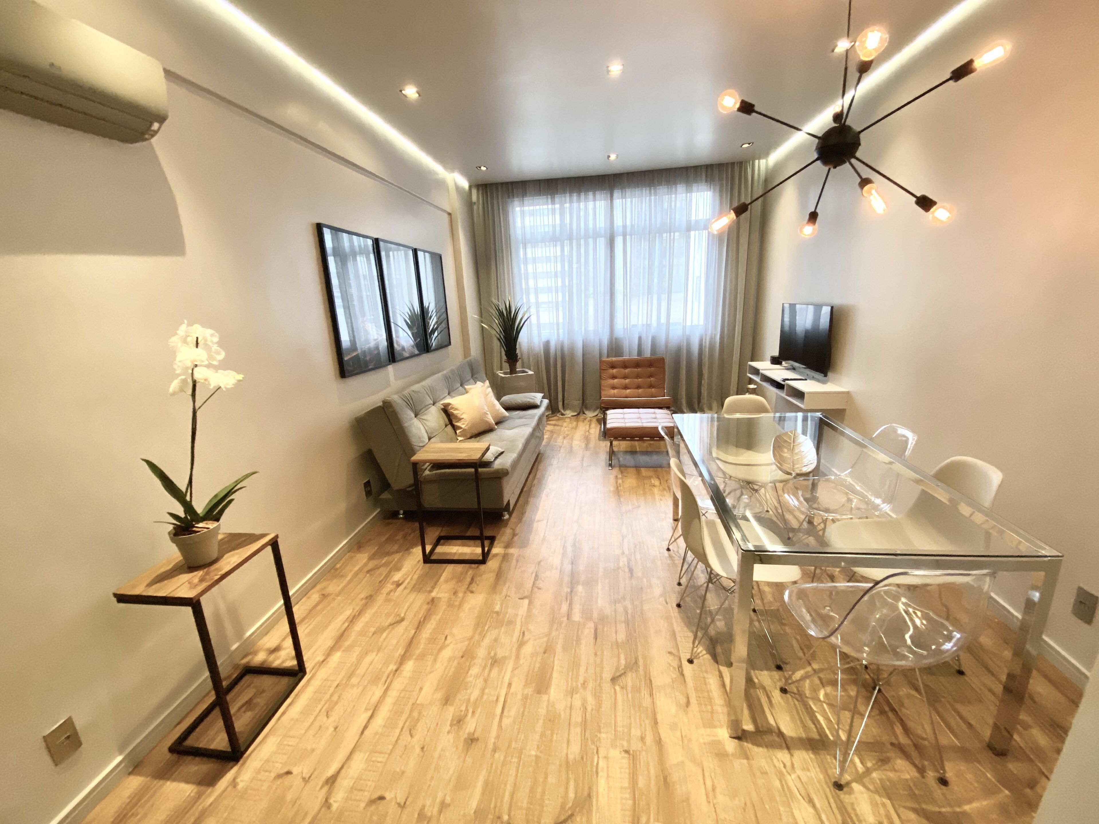 A modern living room with a sofa, dining table, chairs, and a TV.