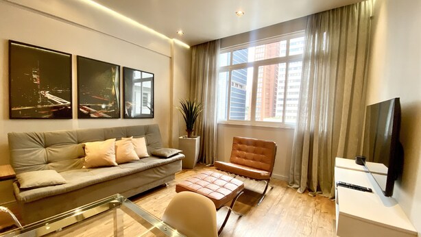 A modern living room with a sofa, a brown leather chair, a glass coffee table, and a TV on a stand.