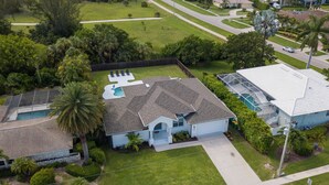 Una casa residencial con piscina, un porche cubierto y un césped bien cuidado.