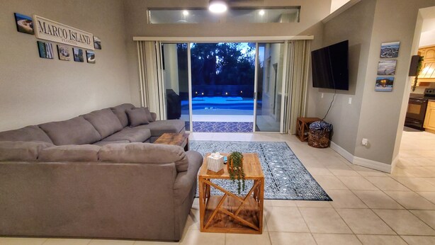 Un moderno salón con un sofá gris, una mesa de centro de madera y vistas a una piscina a través de puertas de cristal.