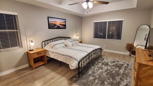 Un dormitorio con cama, mesitas de noche, ventilador de techo, un cuadro en la pared y una ventana con persianas.