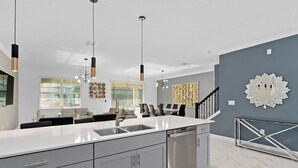 Une cuisine moderne dotée d’un grand îlot central, d’appareils électroménagers en acier inoxydable et de luminaires suspendus.