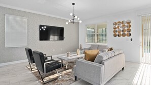 Un salon moderne avec un téléviseur à écran plat, un canapé, une table basse et un lustre.