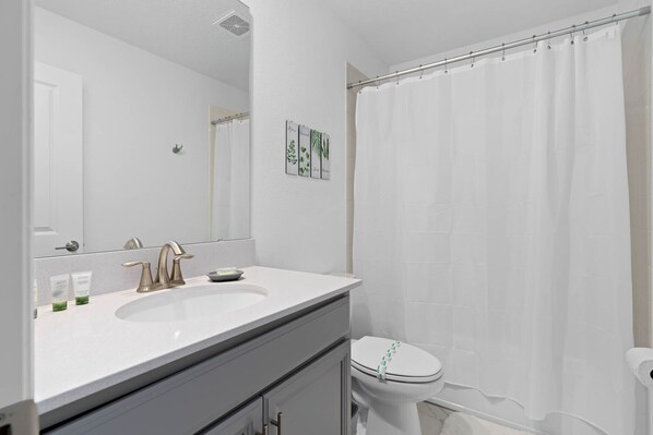 A bathroom with a white sink, a mirror, a toilet, and a shower curtain. - Storey Lake Home 9 Bed 5 Bath (Kissimmee)