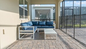 Une terrasse couverte avec un canapé bleu, une table basse blanche et une structure en verre.