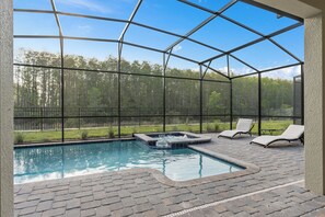 A covered outdoor swimming pool with a hot tub, lounge chairs, and a view of a forest. - Storey Lake Home 9 Bed 5 Bath (Kissimmee)