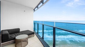 A balcony with a black sofa, a wicker table, and a glass railing overlooking the ocean. - Soul 5 Star Amazing Beachfront 180 Views! (Surfers Paradise)