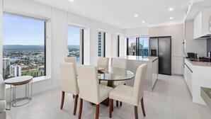 A modern kitchen with a large island, a dining area with a glass table, and large windows offering a city view. - Soul 5 Star Amazing Beachfront 180 Views! (Surfers Paradise)