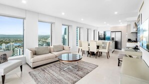 A modern living room with a sofa, coffee table, and dining area, featuring large windows and a city view. - Soul 5 Star Amazing Beachfront 180 Views! (Surfers Paradise)
