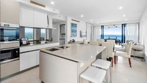 A modern kitchen with a central island, white cabinetry, and built-in appliances. - Soul 5 Star Amazing Beachfront 180 Views! (Surfers Paradise)