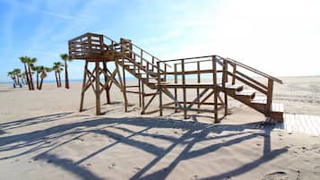Een houten redershutje op een zandstrand, met palmbomen op de achtergrond.