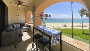 Uma varanda com vista para a praia, um sofá, uma mesa com um vaso de flores e um ventilador de teto.