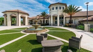 Un patio con una fuente, mobiliario exterior y un edificio con pasillos en arco.